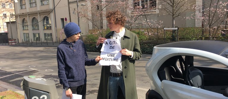 Ein junger Mann und ein Junge stehen neben einem Auto mit einem Zettel auf dem "a cote de" steht.