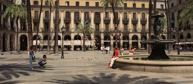 Ein Platz in Barcelona mit einem Brunnen und Palmen.