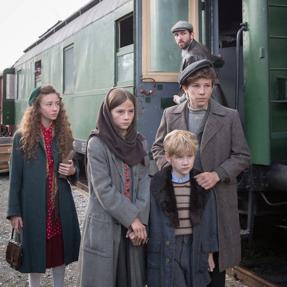 Vier Kinder stehen am Bahnhof neben einem Zug.