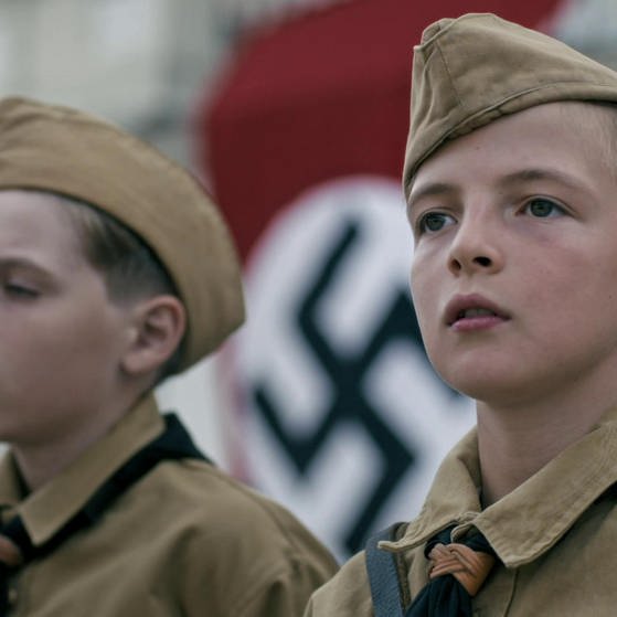 Zwei Jungen in Hitlerjugend-Uniform, im Hintergrund die Hakenkreuzfahne.