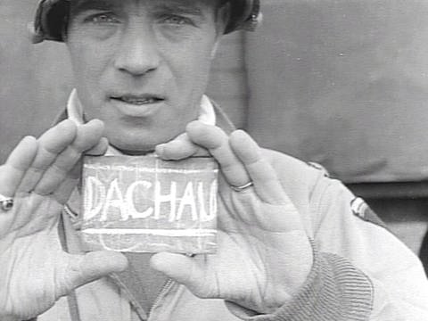 Ein Mann hält ein kleines Schild mit der Aufschrift "Dachau" hoch.