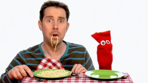 Ein Mann und eine rote Strumpfhandpuppe essen Spaghetti.