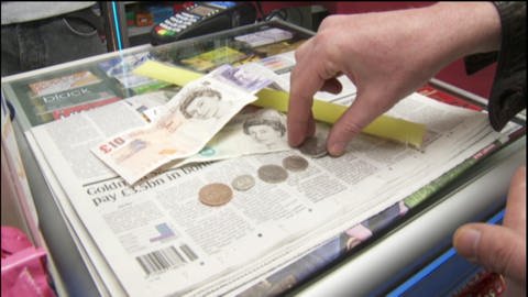 Eine Hand sortiert Münzen und Geldscheine an der Kasse. Es sind englische Pfund.