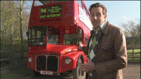 Ein Mann steht vor einem roten Double decker Bus. 