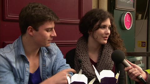 Ein junger Mann und eine junge Frau sitzen zusammen in einem Imbiss und werden interviewt.