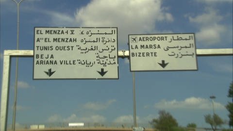 Zwei Straßenschilder. Auf der linken Hälfte sind die Orte auf Französisch ausgeschildert, rechts auf Arabisch. 
