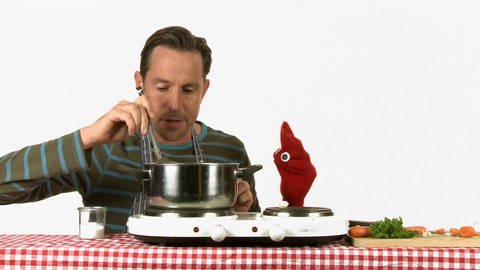 Ein Mann und eine rote Strumpfhandpuppe rühren in einem Topf und kochen Suppe.