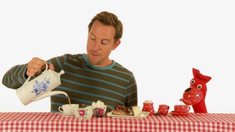 Ein Mann und eine rote Strumpfhandpuppe trinken gemeinsam Tee und essen Kuchen.