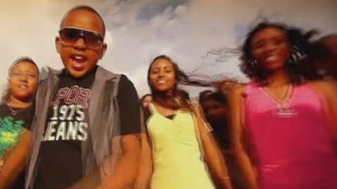 Ein Screenshot aus einem Musikvideo: drei junge Menschen schauen in die Kamera und lachen, ein Junge singt.