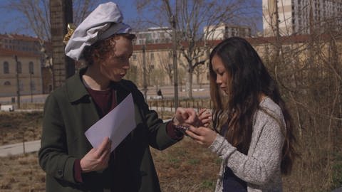 Ein junger Mann mit weißer Mütze zeigt einer Frau etwas auf einem Handy.