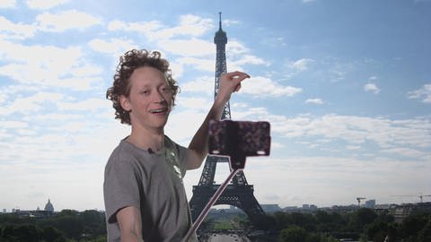 Ein junger Mann filmt sich mit seinem Handy vor dem Eiffelturm.