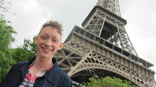 Ein junger Mann steht unterhalb des Eiffelturm.