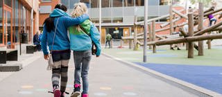 Zwei Freundinnen gehen Arm in Arm über einen Schulhof