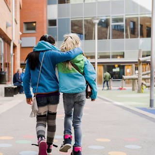 Zwei Freundinnen gehen Arm in Arm über einen Schulhof