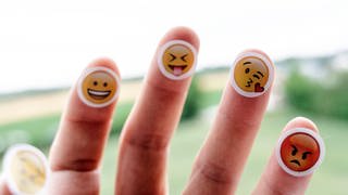 Auf die Finger einer Hand sind verschiedene Emojis aufgeklebt.