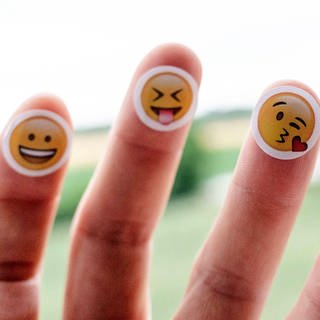 Auf die Finger einer Hand sind verschiedene Emojis aufgeklebt.