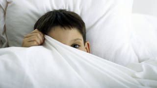 Ein Kind versteckt sich unter einer Bettdecke