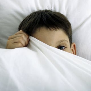 Ein Kind versteckt sich unter einer Bettdecke
