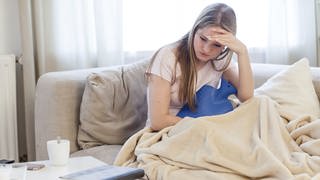 Ein Mädchen sitzt auf einer Couch unter der Decke und wendet traurig den Blick ab