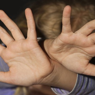 Eine Person hält beide Hände schützend vor ihren Kopf