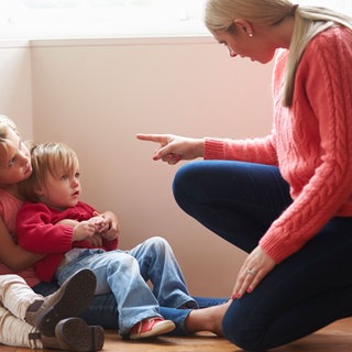 Eine Frau zeigt ermahnend mit dem Zeigefinger auf ein paar Kinder, die ihr gespannt zuhören.