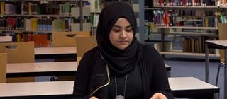 eine Frau mit Kopftuch sitzt in einer Bibliothek