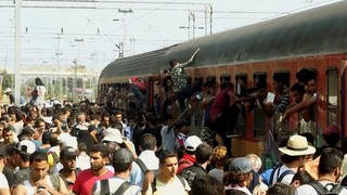 Flüchtlinge klettern von einem überfüllten Bahnsteig in einen ebenso vollen Zug