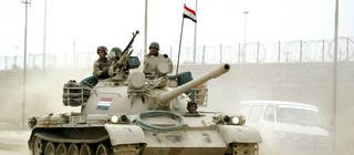 Ein Panzer fährt durch eine staubige Straße in Bagdad, zwei Soldaten schauen hinaus. Internationale Krisen.