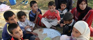 Kinder sitzen im Kreis und essen Brot - Der Alltag der Menschen im Irak ist geprägt von Leid und Krieg. 