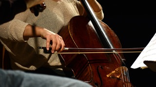 Ein Musiker spielt ein Cello, vor ihr ist ein Notenständer mit Noten zu sehen.