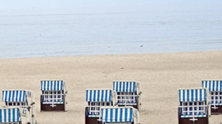 Ein Strand, an dem blau-weiße Strandkörbe stehen.