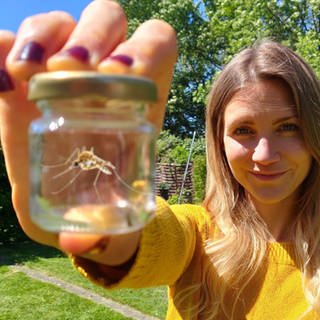 neuneinhalb-Reporterin Jana steht im Garten und zeigt eine Mücke in einem Glas