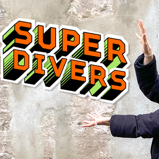 Reporterin Jana vor einer Mauer, sie zeigt auf die Aufschrift "SUPERDIVERS".