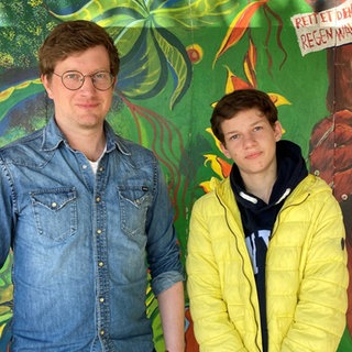 Reporter Robert und Jannis stehen vor einer bunt angemalten Wand in Jannis' Schule.