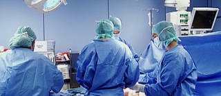 Mehrere Ärzte in blauen Kitteln stehen um einen Patienten.