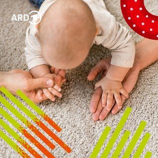 Ein Baby auf dem Boden greift nach den Händen seiner Eltern.