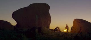Menschen sitzen zwischen Felsen im Sonnenuntergang.