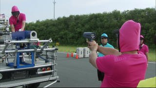Eine Person zielt mit einer Laserpistole zur Geschwindigkeitsbestimmung auf eine Ballwurfmaschine.