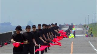 Schwarzgekleidete Personen stehen in einer Reihe und halten rote Fahnen.