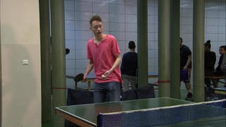 Ein junger Mann steht in einer Turnhalle und spielt Tischtennis.