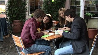 Vier junge Erwachsene sitzen gemeinsam am Tisch und essen.