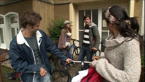 Vier junge Erwachsene stehen mit ihren Fahrrädern vor einem Haus.