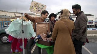 Vier junge Leute stehen an einem Stand auf dem Flohmarkt, vor ihnen viele Kleidungsstücke.