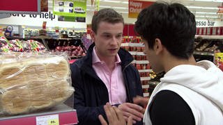 Zwei junge Männer stehen in einem Supermarkt und unterhalten sich mit ernstem Gesichtsausdruck.