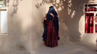 Eine Frau verhüllt sich an einer geschützten Hausecke mit der Burka