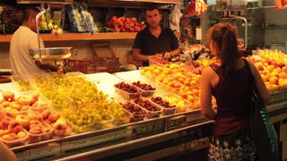 Eine junge Frau steht vor einem Obststand.