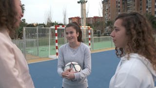 Drei junge Frauen stehen auf einem Fußballplatz.