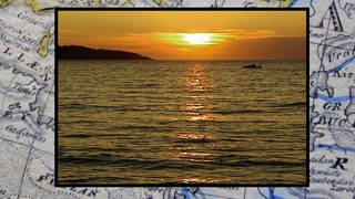 Ein Foto von einem Sonnenuntergang am Meer, im Hintergrund liegt eine Insel. 