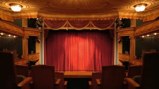 Eine Theaterbühne mit geschlossenem roten Vorhang.