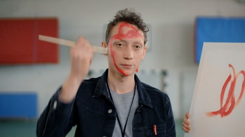 Ein junger Mann bemalt sein Gesicht mit roter Wasserfarbe.